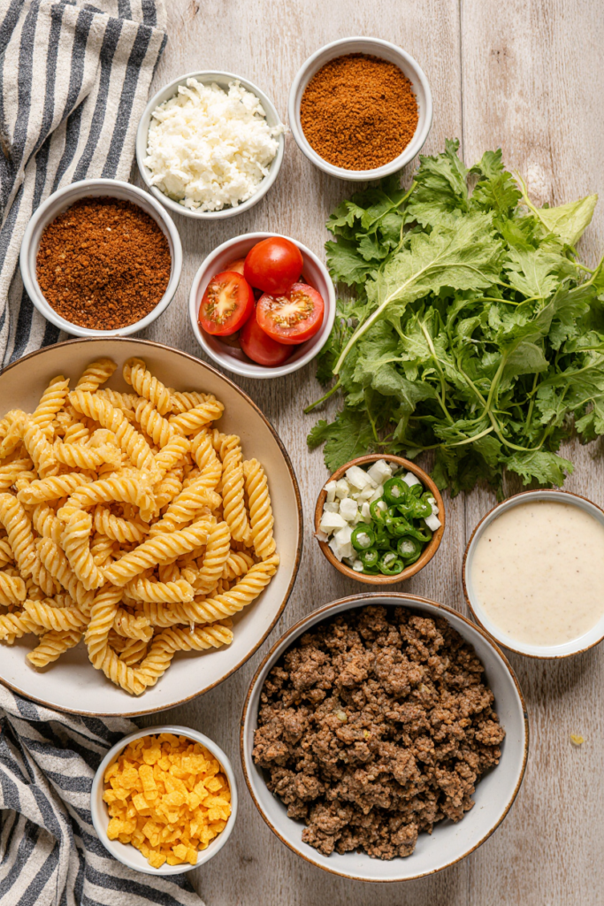 Ingredients for taco pasta salad laid out in bowls on a wooden counter.